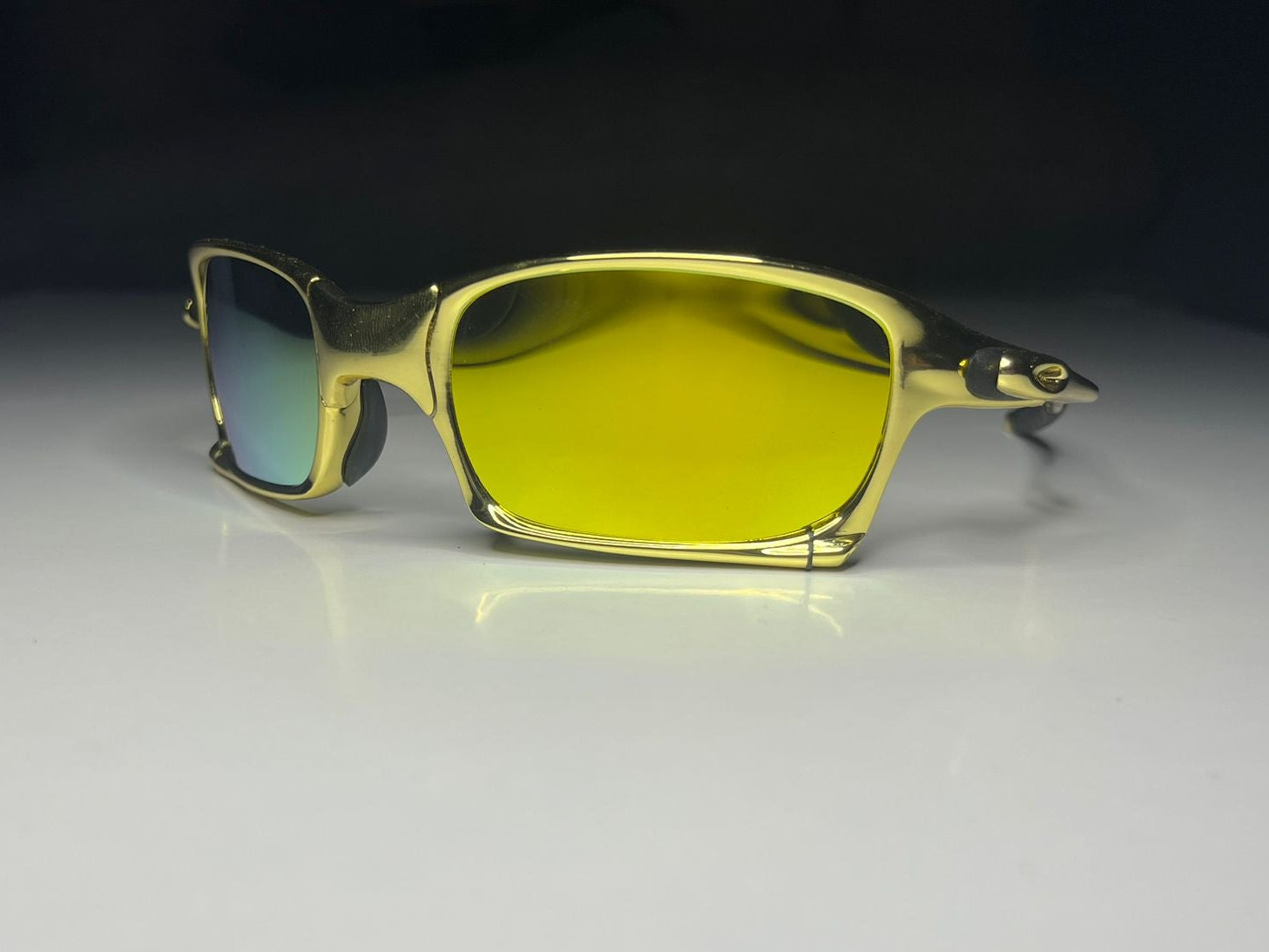 Gold-framed sunglasses with yellow-tinted lenses on a reflective surface.